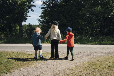 Rear view of sister with brothers standing at roadside during sunny day