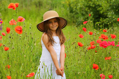 Portrait of young woman standing amidst flowering plants on field