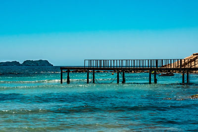 Pier over sea against clear blue sky