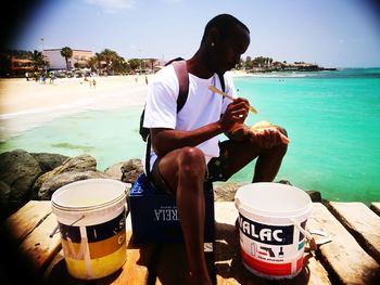 Rear view of man sitting at beach against sky