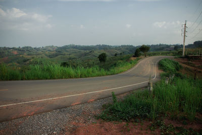 Road passing through field against sky