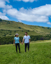 Couple holding hands on field against sky