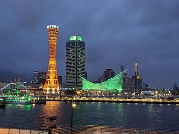 Illuminated buildings by river against sky at night