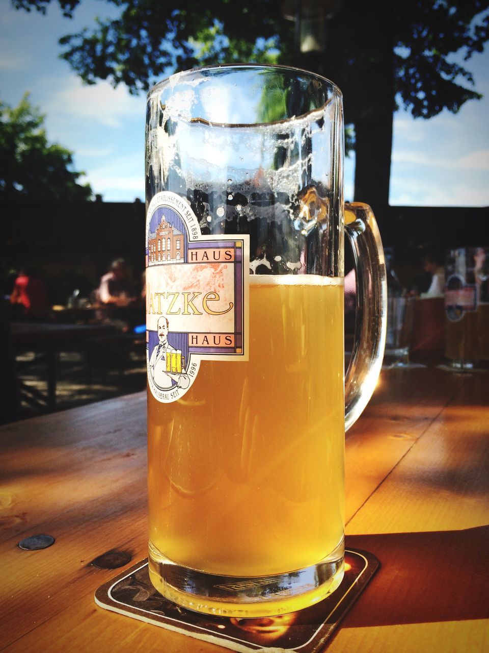 drink, text, food and drink, western script, refreshment, communication, table, drinking glass, tree, close-up, focus on foreground, glass - material, freshness, yellow, incidental people, alcohol, still life, day, outdoors, cafe