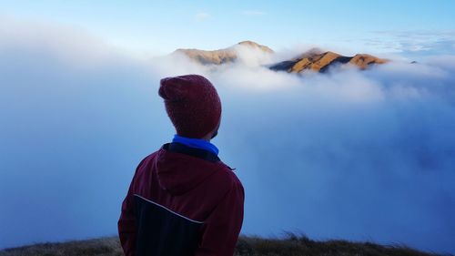 Rear view of man standing by cloudscape on mountain