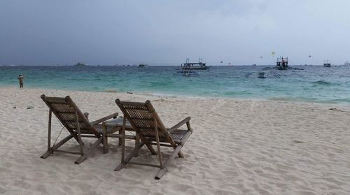 Wooden deck chairs at beach against clear sky