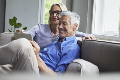 Happy mature couple sitting on couch at home sharing tablet