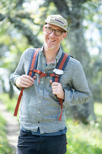 Portrait of smiling hiker with hat, glasses, and backpack outdoors