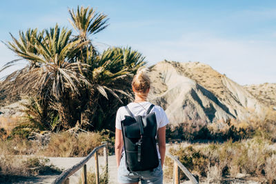 Rear view of woman standing by palm trees against sky