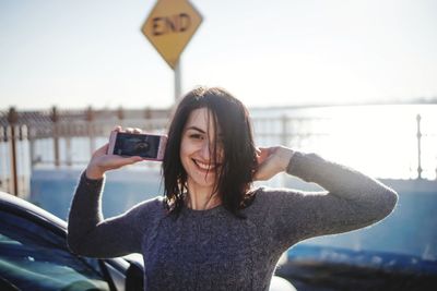 Portrait of young woman using mobile phone against sky