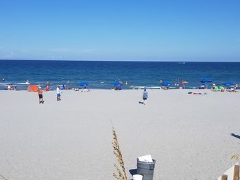 People at beach against clear blue sky