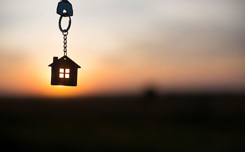 Silhouette of a house figure with a key, a pen with a keychain on the background of the sunset. 