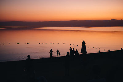 Silhouette people on lake against sky during sunset