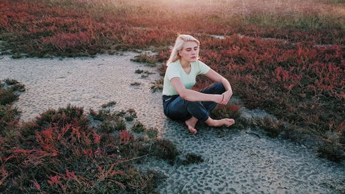 Young woman with cross-legged sitting by grass on field