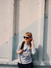 Young woman wearing sunglasses standing against wall