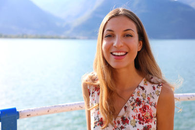 Portrait of smiling young woman standing against mountains and lake