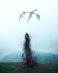 Spooky woman standing on hill against dragon flying in sky