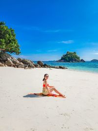 Rear view of woman sitting at beach against clear blue sky