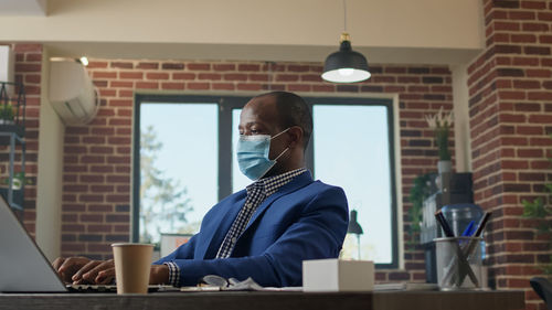 Businessman wearing protective face mask using laptop in office