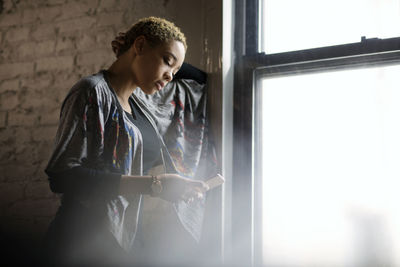 Young woman using smart phone by window at home