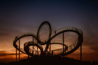 Silhouette of rollercoaster against sky during sunset