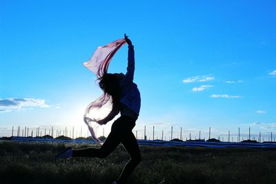 Side view of woman dancing with scarf against blue sky