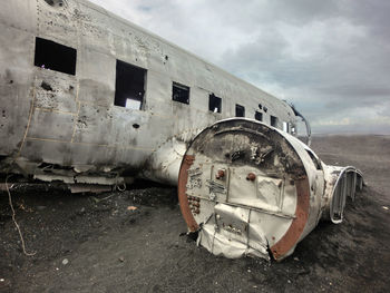 Abandoned airplane on field against cloudy sky