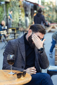 Brutal bearded middle-aged man in a street cafe with a glass of wine