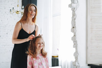 Young mother woman in black dress and little girl daughter in pajamas having fun at home