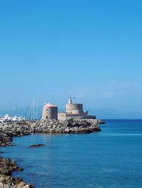 Lighthouse amidst sea and buildings against sky