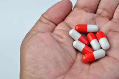 Close-up of hand holding red capsules against white background