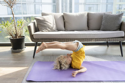 Smiling girl practicing yoga in front of sofa at home