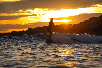 Man jumping in sea against sky during sunset