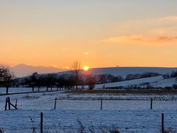 Snow covered field against sky during sunset