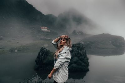 Young woman with hand in hair standing by lake at dusk