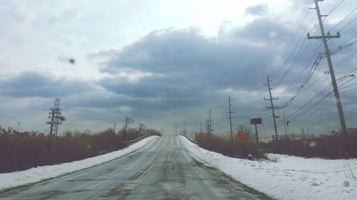 Snow covered road against cloudy sky