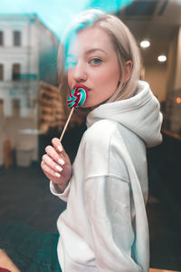 Portrait of young woman eating lollipop seen through window