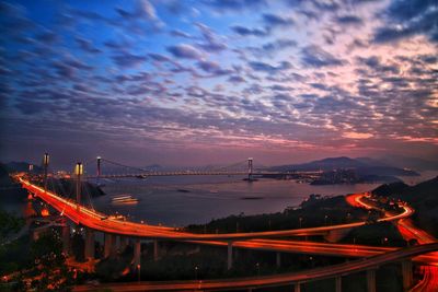 Panoramic view of illuminated city against dramatic sky at sunset