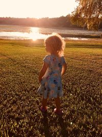 Rear view of woman on field against sky during sunset