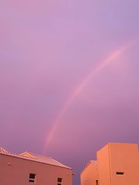 Low angle view of rainbow over buildings against blue sky