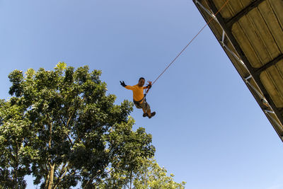 Low angle view of man rappelling against clear sky