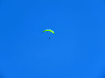 Low angle view of people paragliding against blue sky