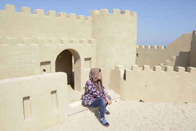 Side view of woman wearing headscarf sitting at old fort