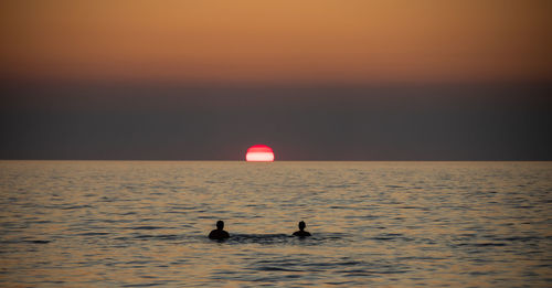 People swimming in sea during sunset