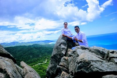 Man sitting on rock against mountains against sky