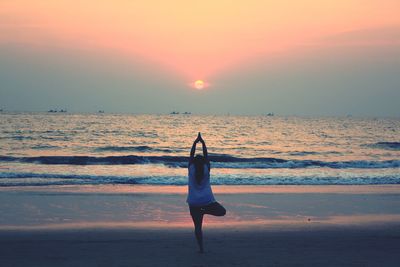 Rear view of man standing at beach during sunset