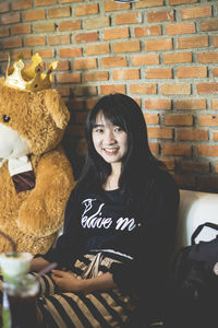 Portrait of smiling young woman standing against brick wall