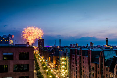 Firework display over illuminated buildings in city at dusk