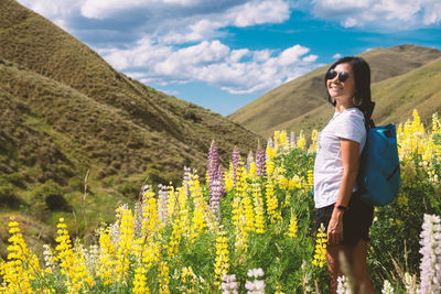 Full length of a oman standing among yellow lupin with mountains and blue sky in background.