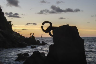 Silhouette man on rock at beach against sky during sunset